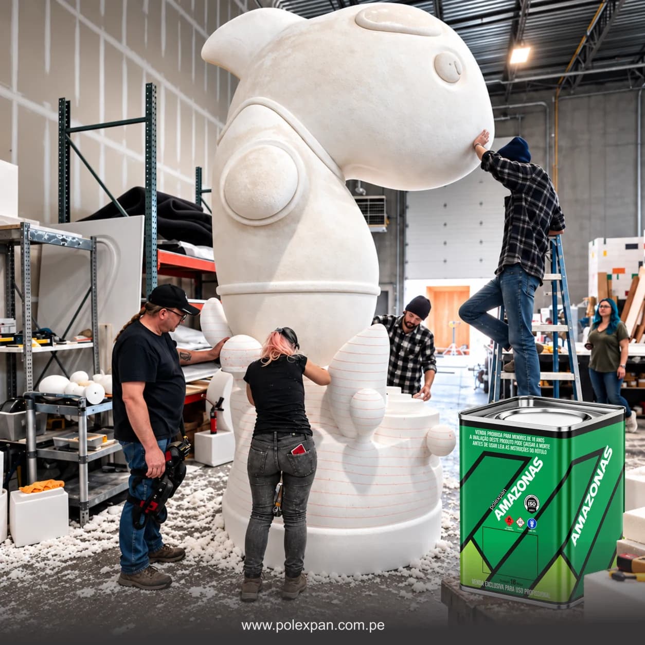 Taller donde un equipo da forma a una escultura gigante de tecnopor, uno de ellos subido a una escalera, con el suelo cubierto de perlas de tecnopor; en primer plano, la lata de 5 galones de pegamento Amazonas.