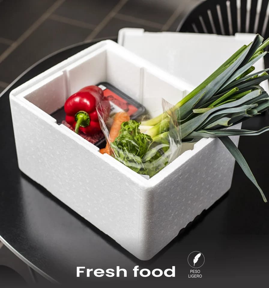 Caja térmica de tecnopor abierta sobre una encimera, con pimientos, zanahorias y cebollas frescas dentro.