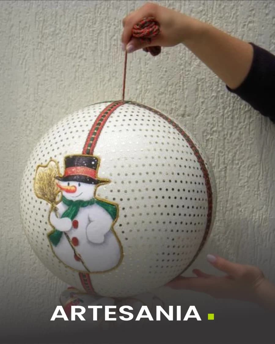 Manos decorando a mano una esfera de tecnopor con la figura de un muñeco de nieve.