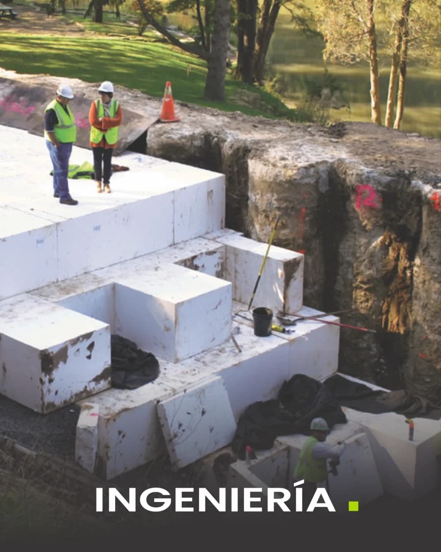Bloques de tecnopor de gran formato apilados dentro de una excavación, con topógrafos al fondo.
