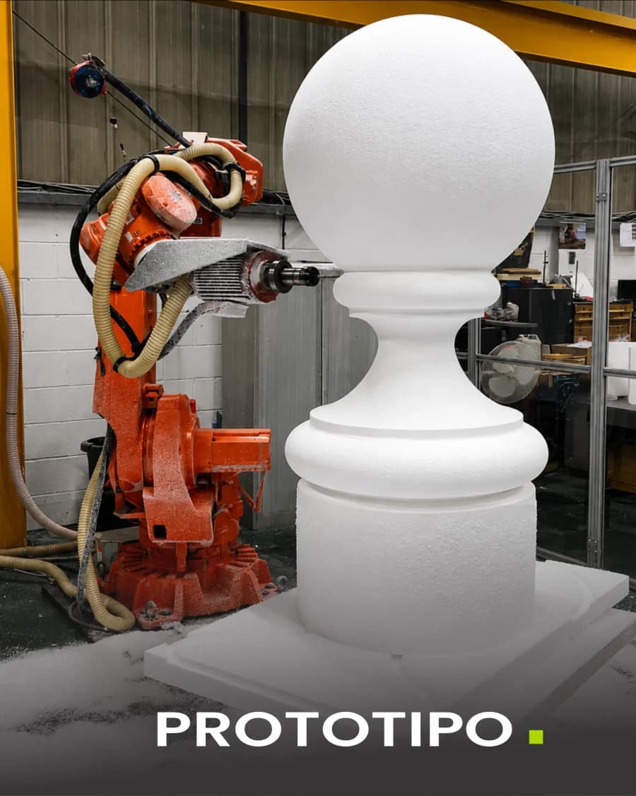 Brazo robótico tallando un balaustre de tecnopor a tamaño real en un taller.