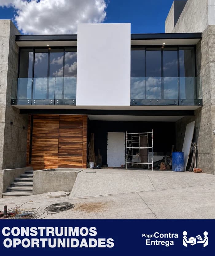 Fachada de una vivienda moderna con cochera y portón de madera. Al pie, los rótulos «Construimos oportunidades» y «Pago contra entrega».